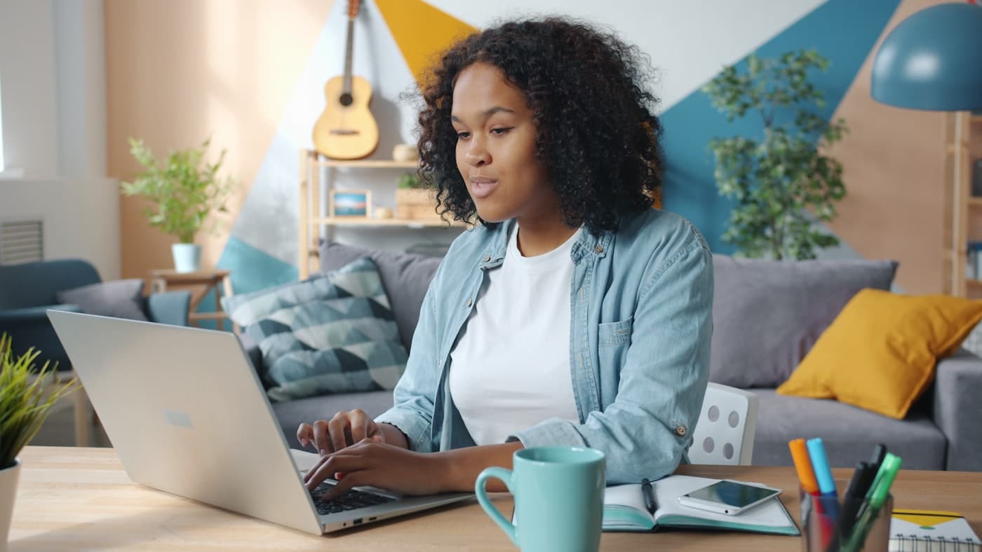 Someone working on a laptop at a desk at home, with a notebook and coffee beside them